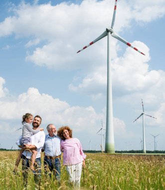 Multigeneration family standing on field on wind farm. clipart