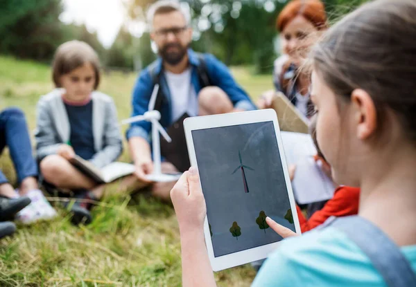 Group of school children with teacher and windmill model on field trip in nature.