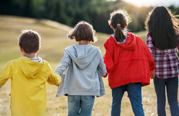 Pandangan belakang tentang sekelompok anak-anak sekolah yang berjalan-jalan di lapangan . — Stok Foto