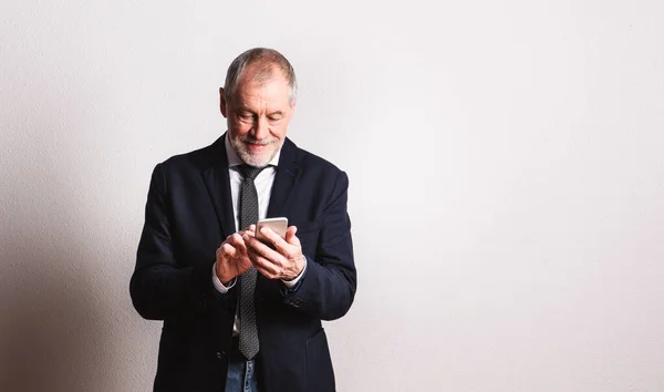 Portrét staršího muže s chytrým telefonem ve studiu, textové zprávy. — Stock fotografie