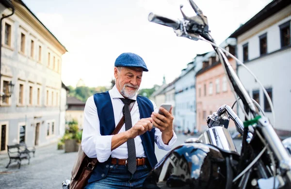 Un homme d'affaires senior avec une moto en ville, en utilisant un smartphone . — Photo
