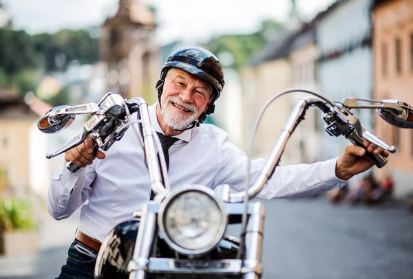 A senior businessman with motorbike in town, looking at camera. — Stock Photo, Image
