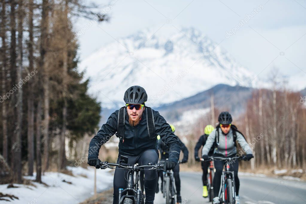 Group of mountain bikers riding on road outdoors in winter.