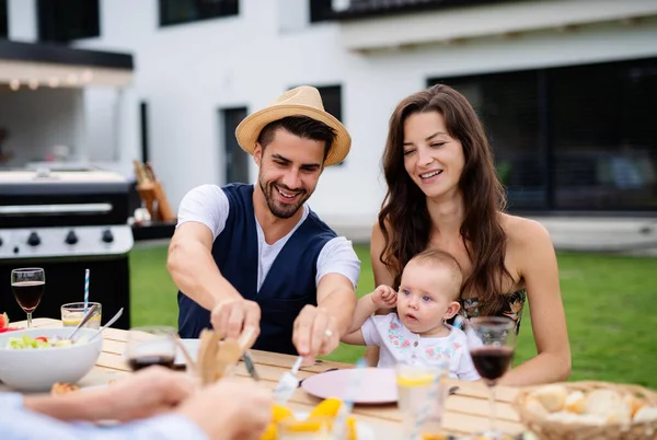 Jovem casal com bebê sentado à mesa ao ar livre no churrasco do jardim da família . — Fotografia de Stock