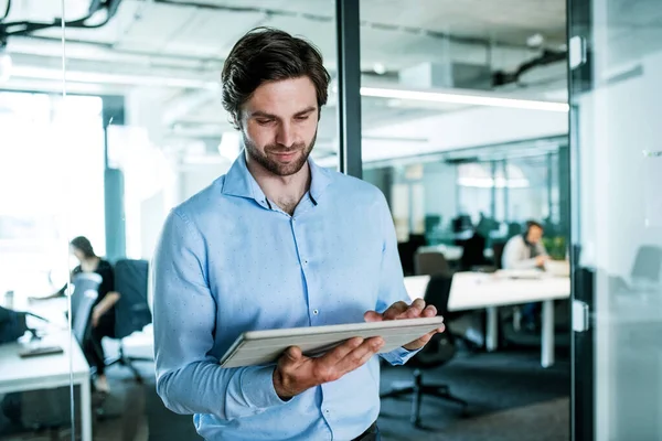 Ritratto di giovane uomo d'affari con tablet in piedi in un ufficio, al lavoro . — Foto Stock