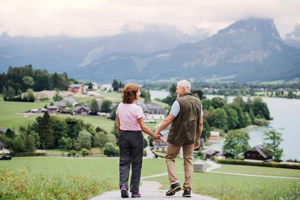 Blick von hinten auf Rentnerehepaar beim Wandern in der Natur, Händchen haltend. — Stockfoto