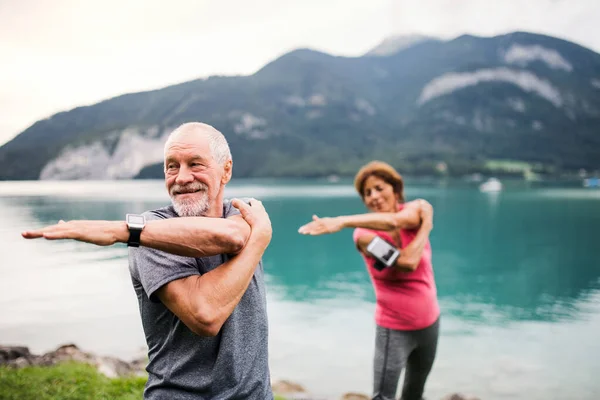 Старша пара пенсіонерів зі смартфоном на озері в природі, здійснює вправи . — стокове фото