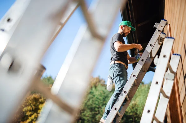 Una vista laterale di uomo maturo all'aperto in estate, pittura casa in legno . — Foto Stock