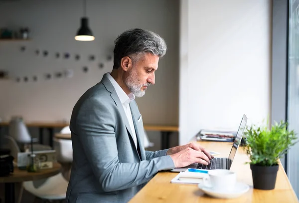 Uomo maturo con computer portatile a tavola in un caffè, al lavoro . — Foto Stock