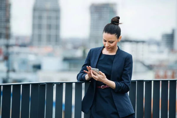 Una giovane donna d'affari in piedi su una terrazza, utilizzando lo smartphone . — Foto Stock