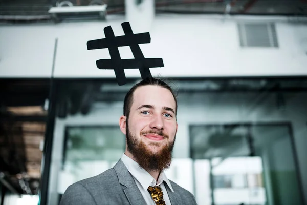 Porträt eines jungen Geschäftsmannes, der in einem Büro steht und ein Hashtag-Stirnband trägt. — Stockfoto