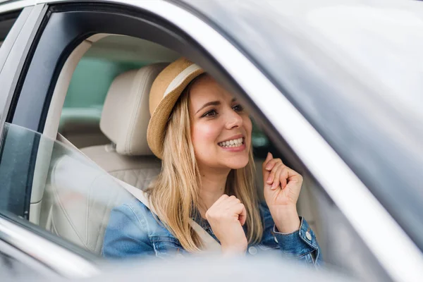 Young woman with hat sitting in car, listening to music and dancing. — Stock Photo, Image