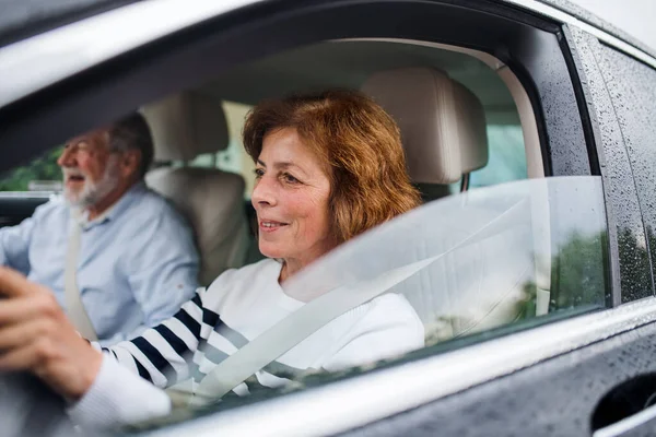 Feliz pareja de ancianos sentados en el coche, conduciendo y hablando . — Foto de Stock