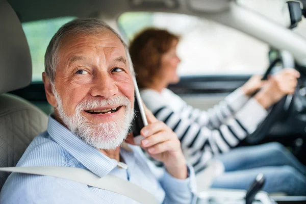 Feliz pareja de ancianos con teléfono inteligente sentado en el coche, va de viaje . — Foto de Stock