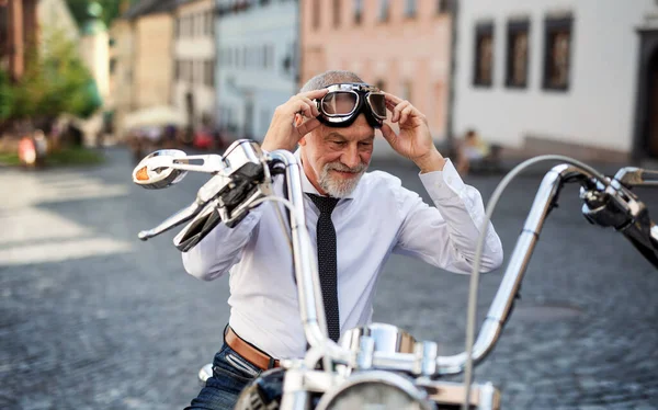 Um empresário sênior com moto na cidade, colocando óculos . — Fotografia de Stock