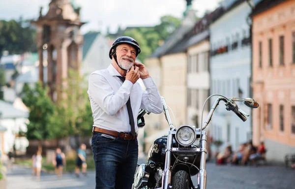 Старший бизнесмен с мотоциклом в городе, надевающий шлем . — стоковое фото