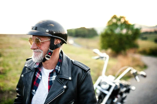 Ένας χαρούμενος ηλικιωμένος ταξιδιώτης με μοτοσικλέτα στην ύπαιθρο, περπατώντας. — Φωτογραφία Αρχείου