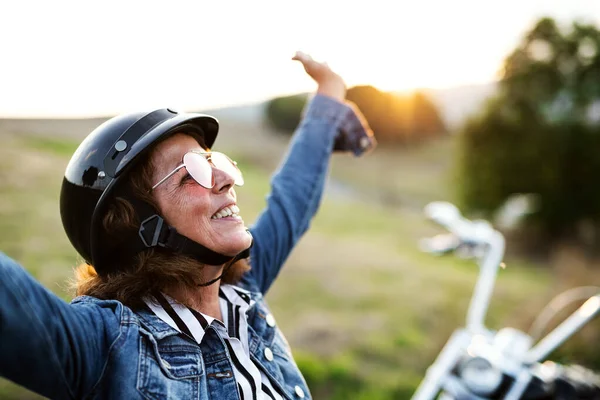 Wesoły starszy kobieta podróżnik z motocyklem na wsi. — Zdjęcie stockowe