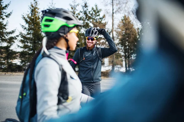 Skupina horských cyklistů stojí na silnici venku v zimě, mluví. — Stock fotografie