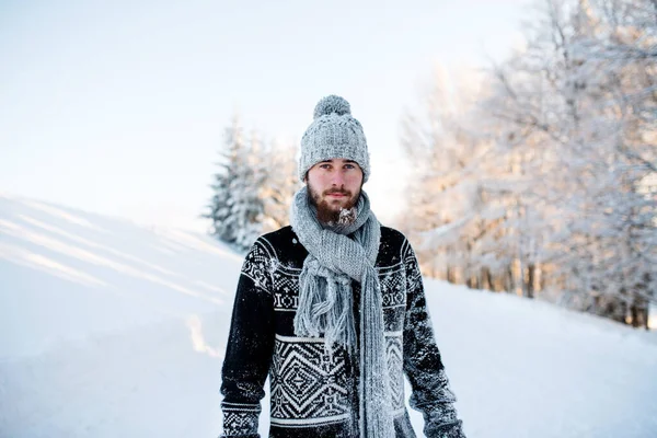 Junger Mann steht im Winter draußen im Schnee und blickt in die Kamera. — Stockfoto