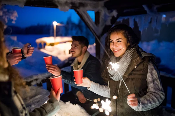 Grupo de jóvenes amigos al aire libre en la nieve en invierno por la noche, la celebración de bengalas . — Foto de Stock