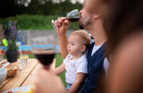 Junges Paar mit Baby sitzt auf Familienfeier am Tisch im Freien und trinkt Wein. — Stockfoto