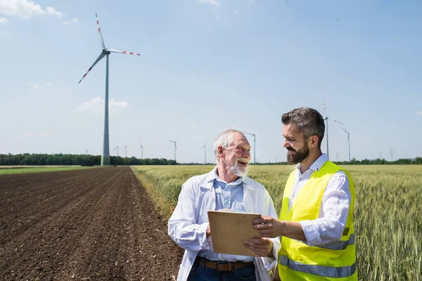 Inżynierowie stojący na farmie wiatrowej, czyniąc notatki. — Zdjęcie stockowe