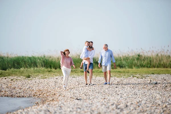 Famiglia multigenerazionale in vacanza passeggiando lungo il lago, tenendosi per mano . — Foto Stock