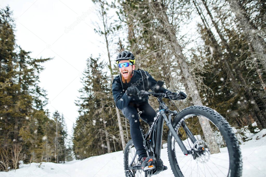 Side view of mountain biker riding in snow outdoors in winter nature.