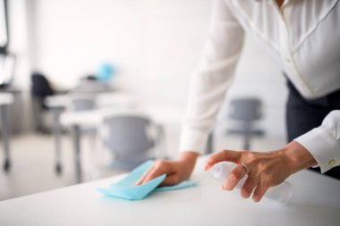 Öğretmen, 19 numaralı karantina ve tecrit sonrası okulda masaları dezenfekte ediyor..