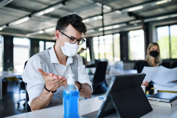 Young people with face masks back at work in office after lockdown, disinfecting hands. — Stock Photo, Image