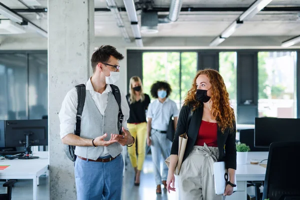 Young people with face masks back at work in office after lockdown, talking. — Stock Photo, Image