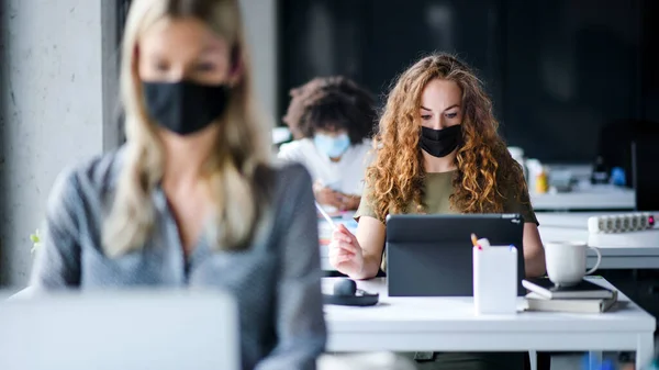 Mladí lidé s obličejovými maskami zpět v práci nebo ve škole v úřadu po uzavření. — Stock fotografie