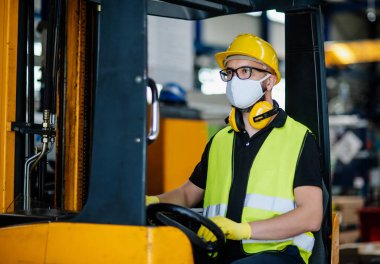 Koruyucu maskeli forklift şoförü endüstriyel fabrikada ya da depoda çalışıyor..