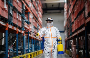 Man worker with protective mask and suit disinfecting industrial factory with spray gun. clipart