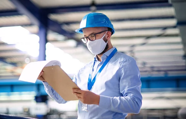 Técnico o ingeniero con máscara protectora y casco trabajando en fábrica industrial . — Foto de Stock