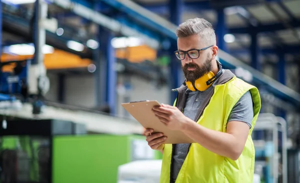 Técnico ou engenheiro com fones de ouvido de proteção em pé na fábrica industrial . — Fotografia de Stock