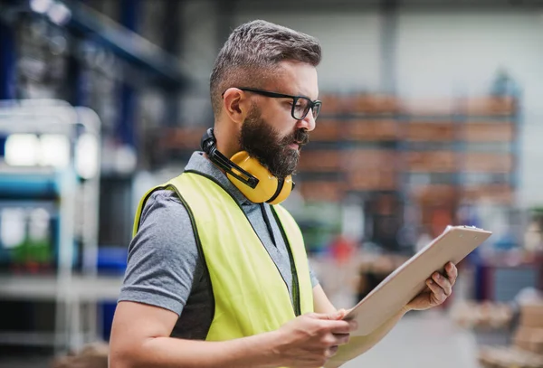 Teknisi atau insinyur dengan headphone pelindung berdiri di pabrik industri. — Stok Foto