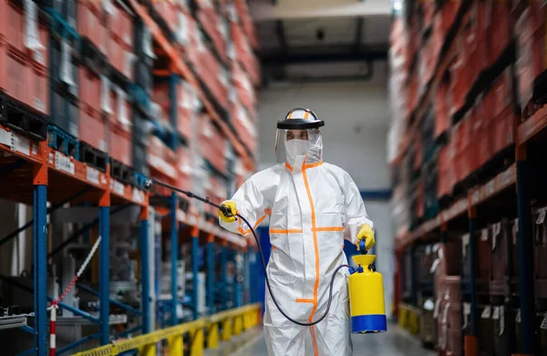 Hombre trabajador con máscara protectora y traje desinfectando fábrica industrial con pistola pulverizadora . —  Fotos de Stock