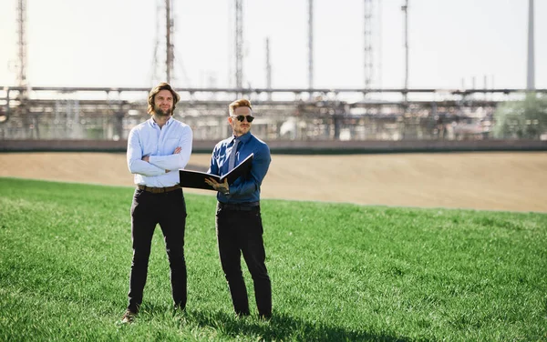 Dos jóvenes ingenieros de pie al aire libre por la refinería de petróleo, discutiendo temas . — Foto de Stock