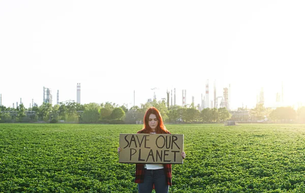 Młoda aktywistka z tabliczką stojąca na zewnątrz przy rafinerii ropy, protestująca. — Zdjęcie stockowe