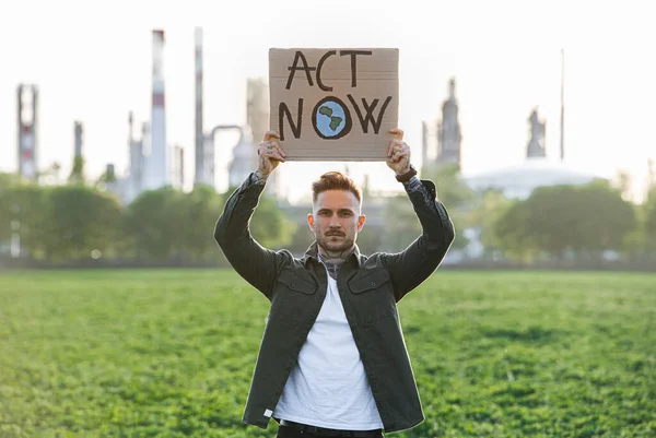 Young activist with placard standing outdoors by oil refinery, protesting. — Stock Photo, Image