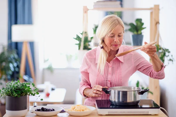 Mujer mayor cocinando en la cocina en el interior, revolviendo pasta en olla . —  Fotos de Stock