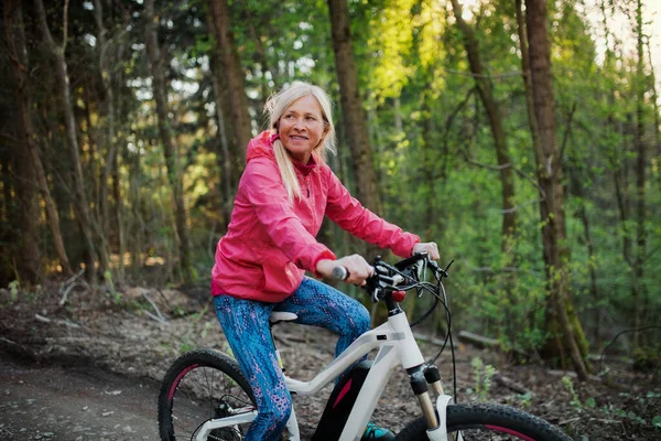 Aktive Seniorin mit E-Bike in der Natur unterwegs. — Stockfoto