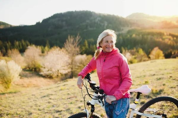 Active senior woman with bicycle outdoors in nature, resting.