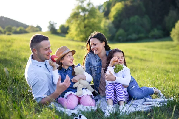 Szczęśliwa rodzina z dwiema małymi córkami siedzącymi na świeżym powietrzu w wiosennej przyrodzie, mającymi piknik. — Zdjęcie stockowe