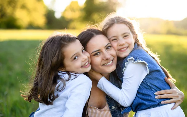 Moeder met twee kleine dochters hebben plezier buiten in de lente natuur, knuffelen. — Stockfoto