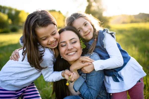 Moeder met twee kleine dochters hebben plezier buiten in de lente natuur, knuffelen. — Stockfoto