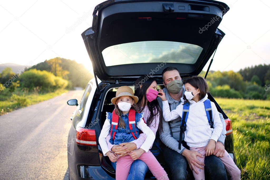 Family with two small daughters on trip outdoors in nature, wearing face masks.