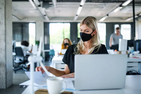 Jovem com máscara facial de volta ao trabalho no escritório após o bloqueio, trabalhando . — Fotografia de Stock